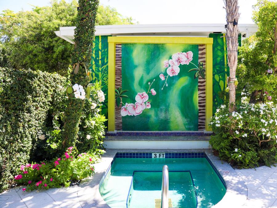A pool area with a green and yellow mural, surrounded by lush greenery and flowering plants.