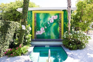 A pool area with a green and yellow mural, surrounded by lush greenery and flowering plants.