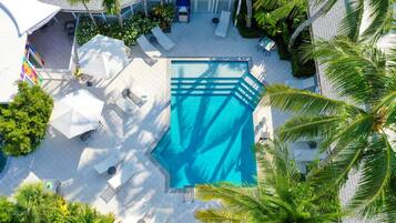 An aerial view of a hotel courtyard with a swimming pool, lounge chairs, umbrellas, and palm trees.