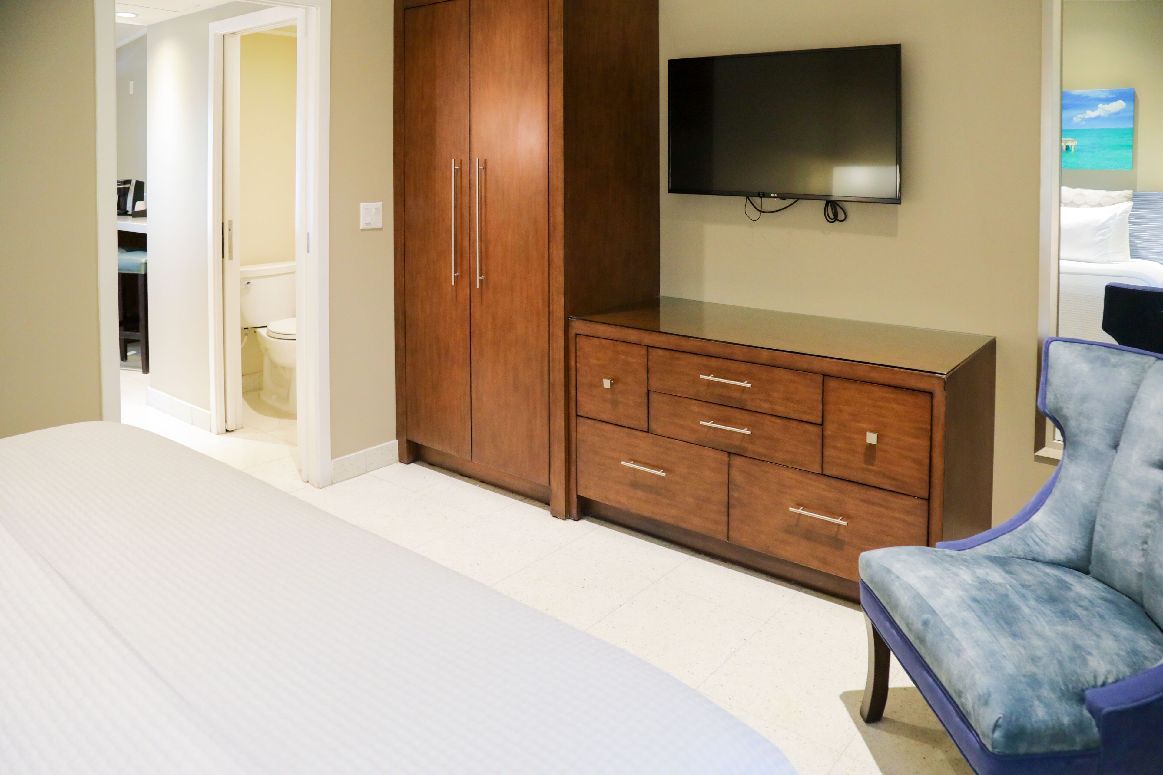 A bedroom with a bed, wooden wardrobe, a flat-screen TV, and a blue armchair.