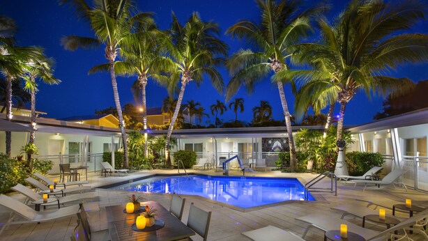 A pool area with lounge chairs and a table, surrounded by palm trees. - Orchid Key Inn - Adults Only (Key West)