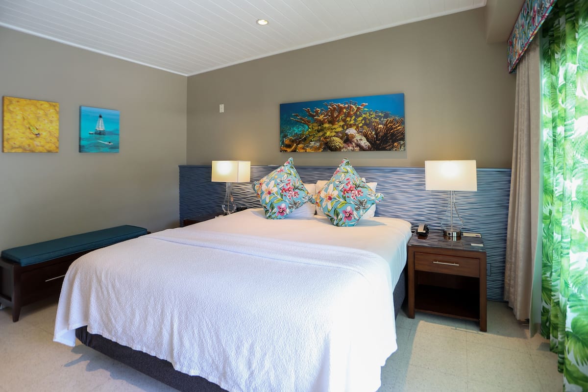 Quarto de hotel com uma cama grande, duas mesas de cabeceira, um banco e obras de arte nas paredes.