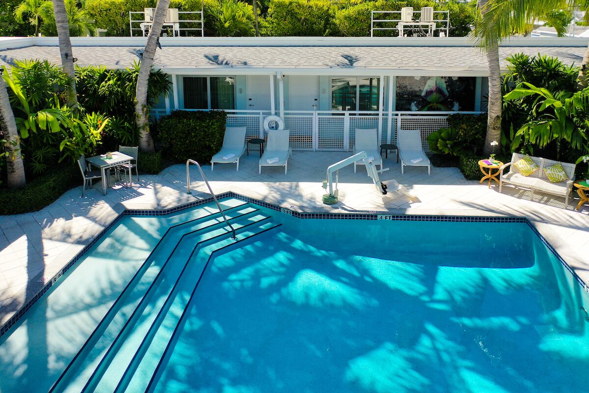 A swimming pool with lounge chairs and a covered seating area, surrounded by palm trees and greenery.