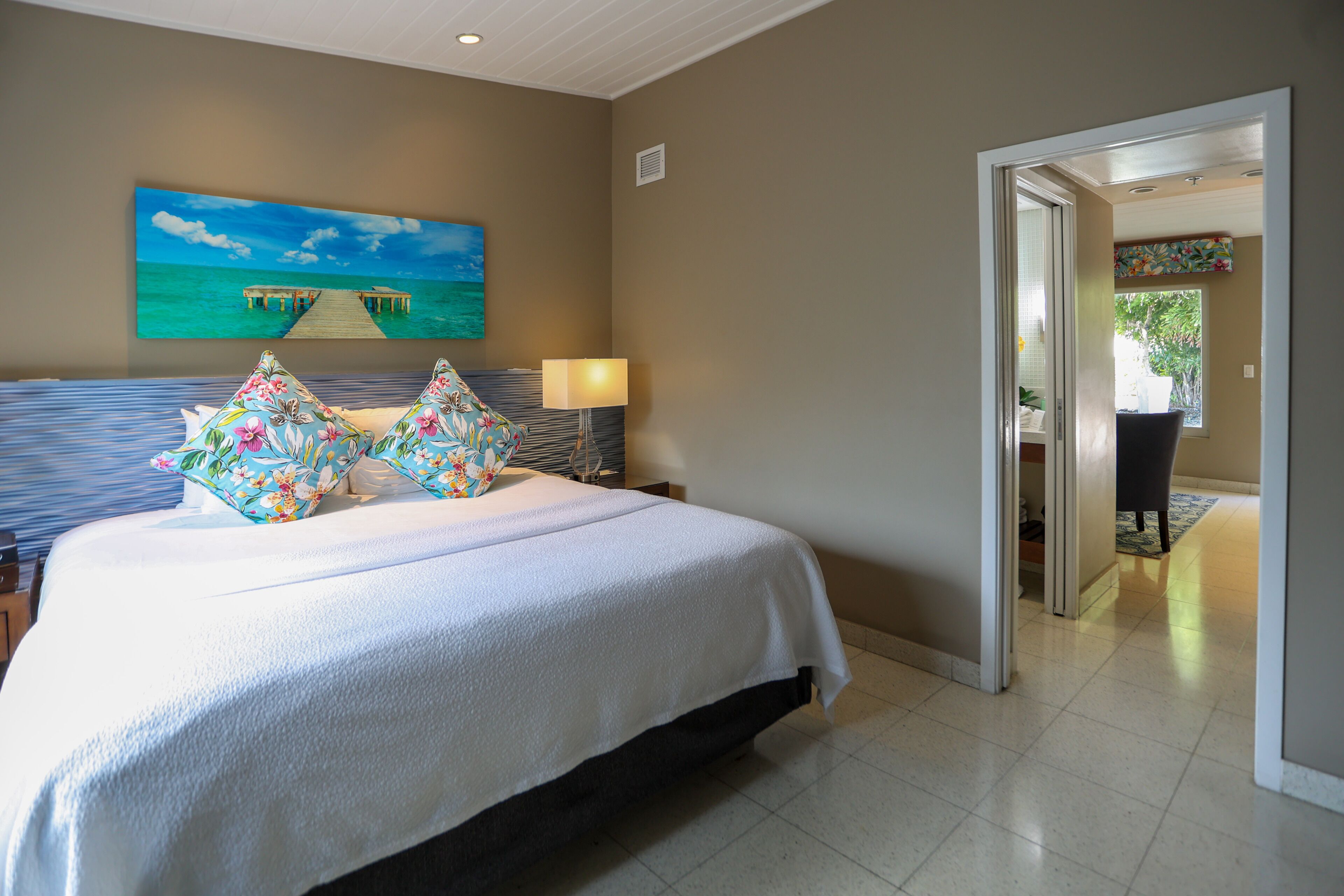 Un dormitorio con una cama grande, un cuadro de un muelle y vistas a un balcón desde una puerta abierta.