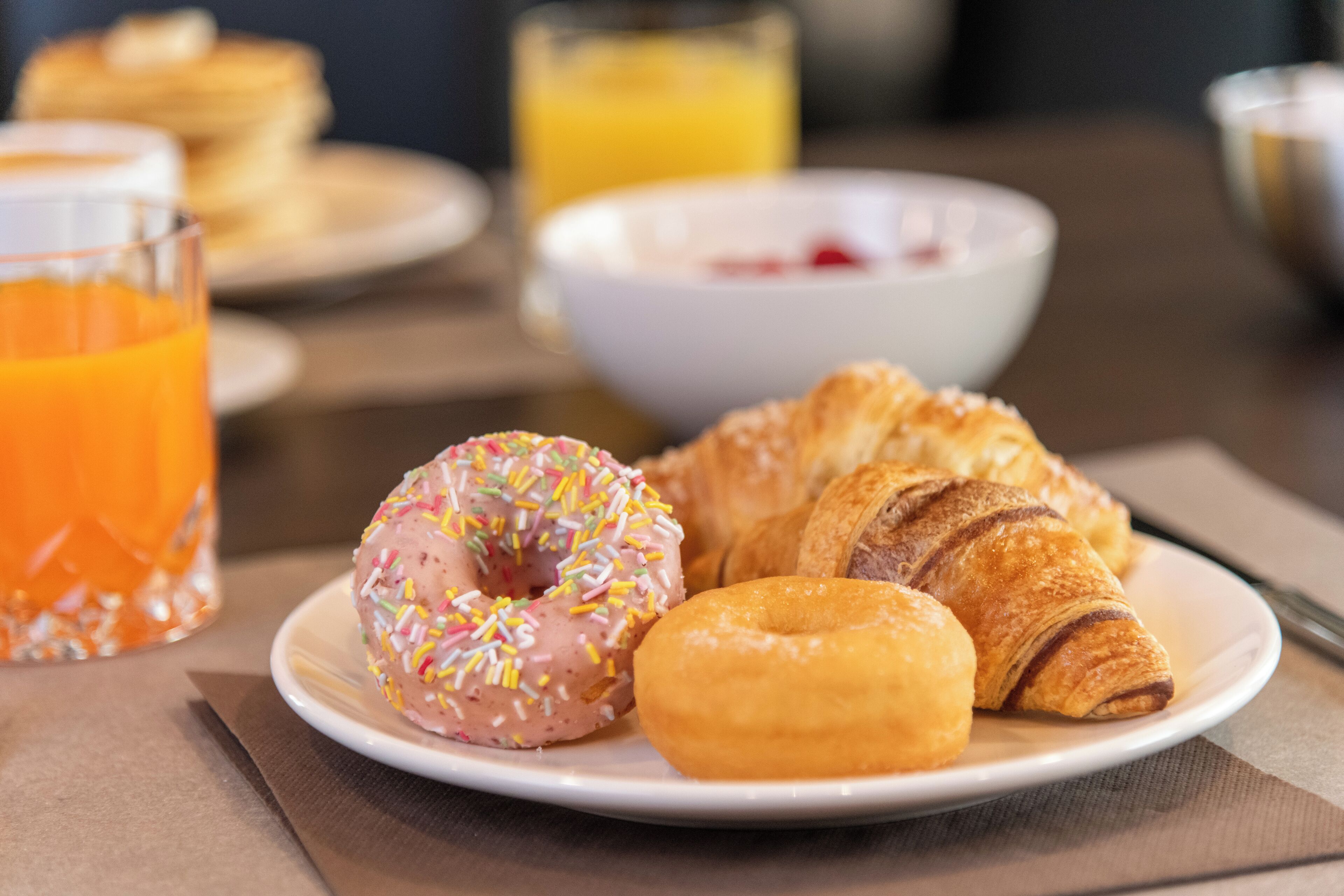 Een ontbijtbord met een roze glazuurdonut, een gewone donut en een croissant.