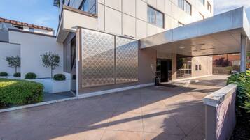 A modern building with a covered entrance, a tiled courtyard, and a patterned wall.