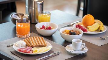 Esmorzar amb torrades, ous, bacon i fruita als plats, un bol de cereals, un got de suc d'aranja i una tassa de cafè.