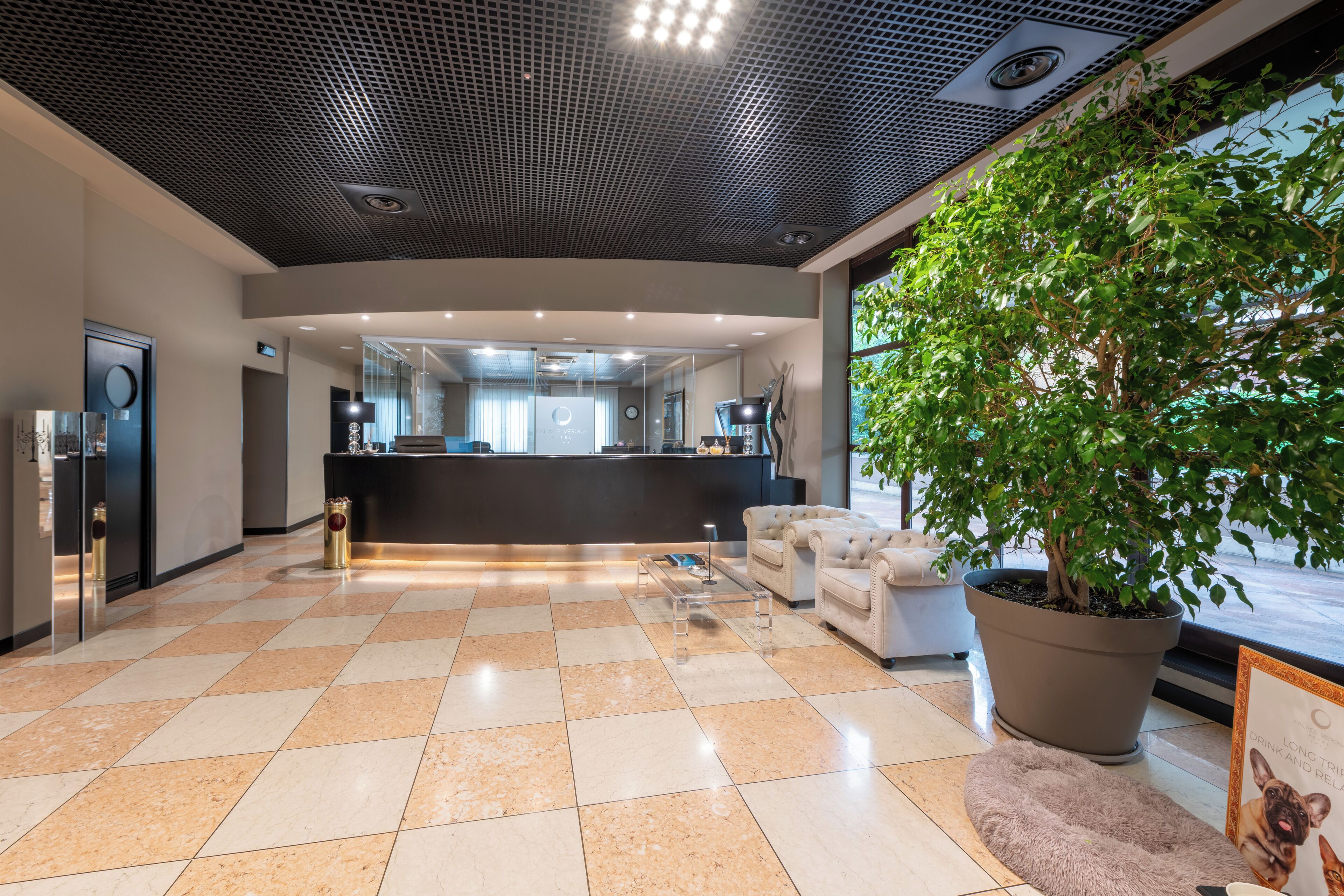 A spacious lobby with a checkered floor, a reception desk, a potted tree, and a sofa.