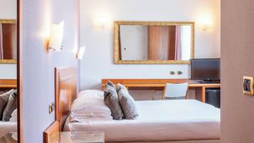 A hotel room with a bed, a desk with a chair, a television, and a large mirror on the wall.