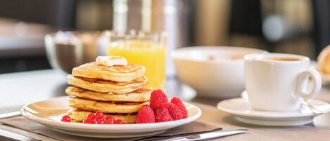 A breakfast setting with pancakes, raspberries, a glass of orange juice, and a cup of coffee on a table.