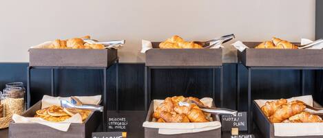 A breakfast buffet with labeled boxes of pancakes, brioche, and croissants.