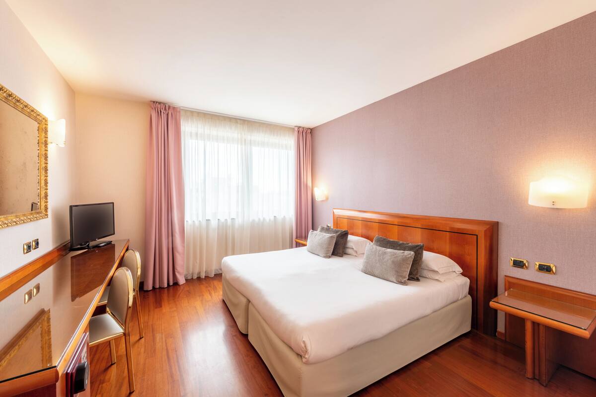 A hotel room with a large bed, a desk with a television, and a nightstand.