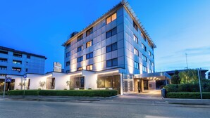 Un hôtel moderne, avec un bâtiment d’angle, de grandes fenêtres et une entrée bien éclairée.