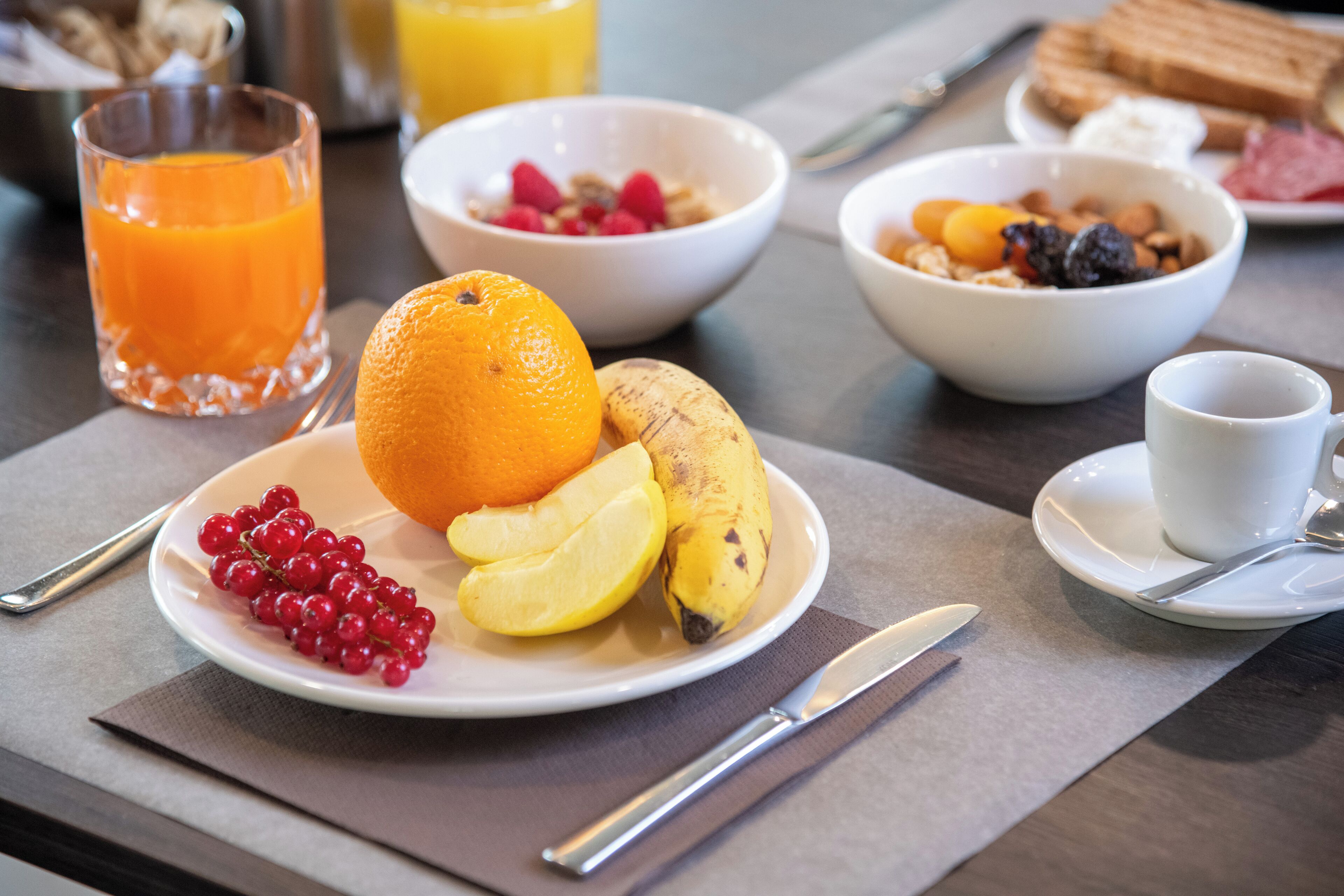 Een ontbijtsetting met een bord fruit, een glas sinaasappelsap en een kom ontbijtgranen.