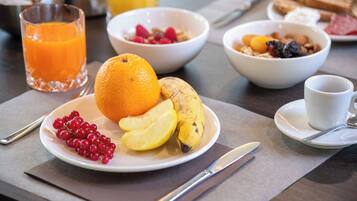 Een ontbijtsetting met een bord fruit, een glas sinaasappelsap en een kom ontbijtgranen.
