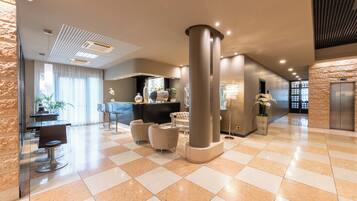 A spacious lobby with a checkered floor, modern furniture, a reception desk, and a large pillar.