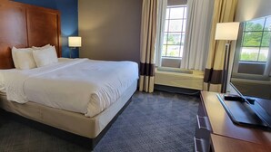A hotel room with a large bed, two bedside lamps, a desk with a computer and remote control, a window with curtains, and an air conditioning unit. - Comfort Inn Bessemer Birmingham South (Bessemer)