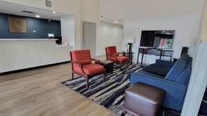 A hotel lobby with a reception desk, two red armchairs, a blue sofa, a television, and a patterned rug. - Comfort Inn Bessemer Birmingham South (Bessemer)