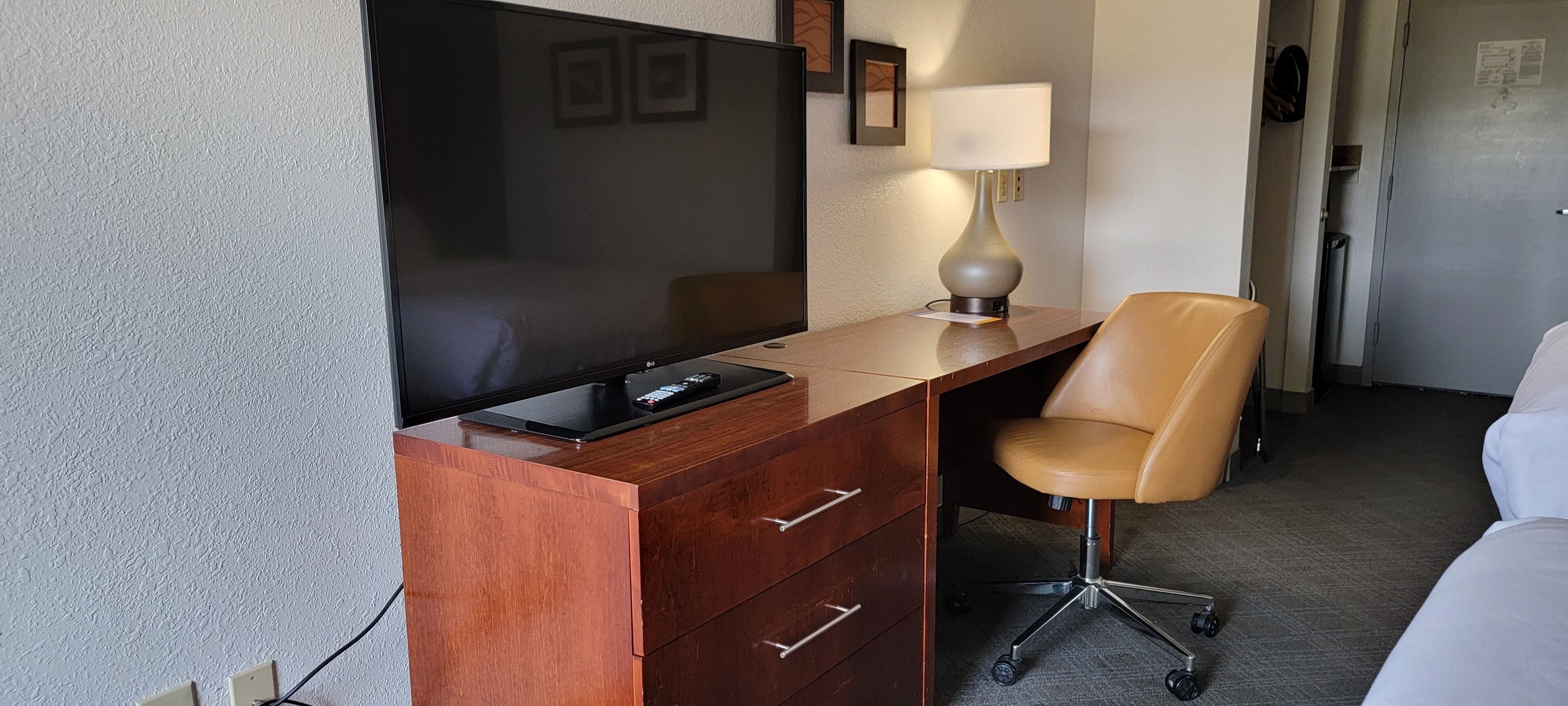 Una camera d'albergo con una scrivania in legno, una poltrona in pelle, una TV a schermo piatto e una lampada.