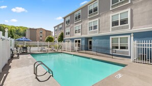 A swimming pool with a white fence, lounge chairs, and a building with multiple windows and a blue accent wall.