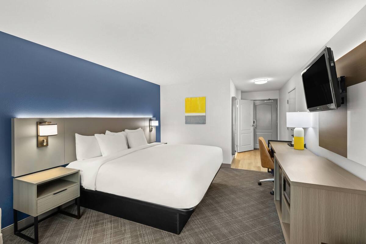 Habitación de hotel con una cama grande, mesita de noche, lámpara, escritorio y televisor.