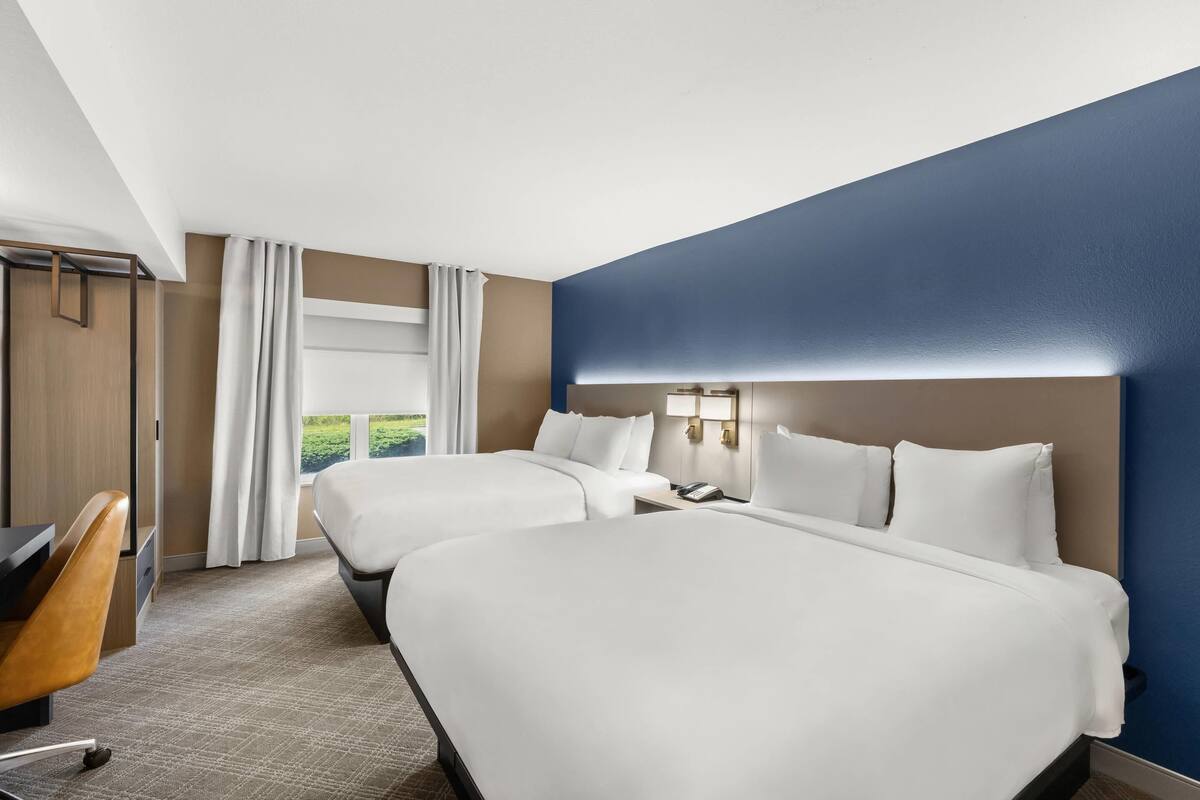 Habitación de hotel con dos camas, un escritorio y vistas a zonas verdes.