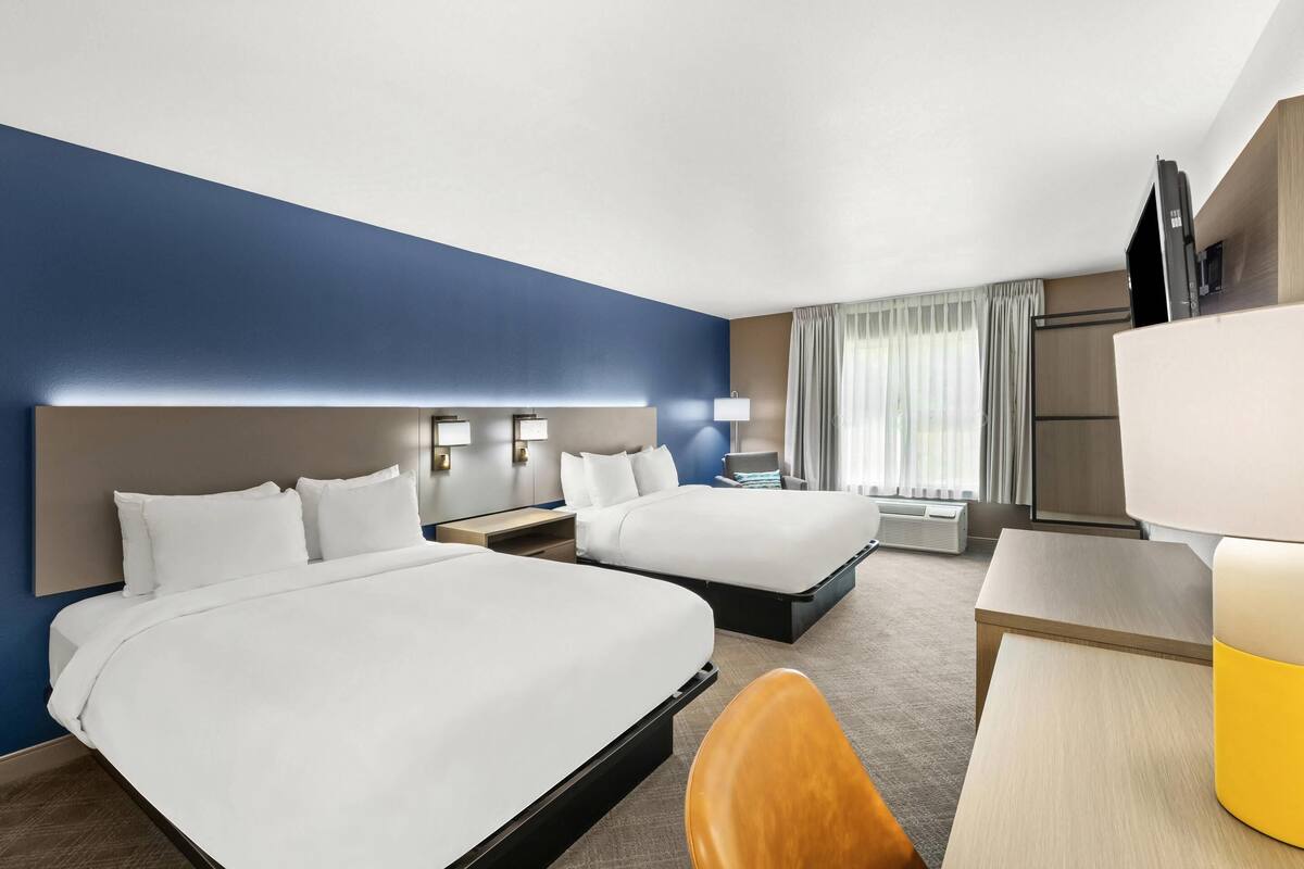 Habitación de hotel con dos camas, un escritorio, una silla y un televisor.