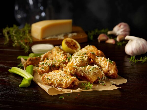 A plate of chicken wings garnished with cheese and herbs, accompanied by a lemon half and garlic cloves on a wooden table. - Radisson Hotel Panama Canal (Panama City)