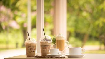 Una mesa con tres cafés helados y una taza blanca, sobre un fondo verde desenfocado.