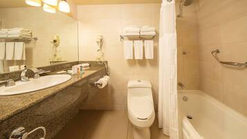 A bathroom with a sink, toilet, and shower. There are towels and a hairdryer on the wall.