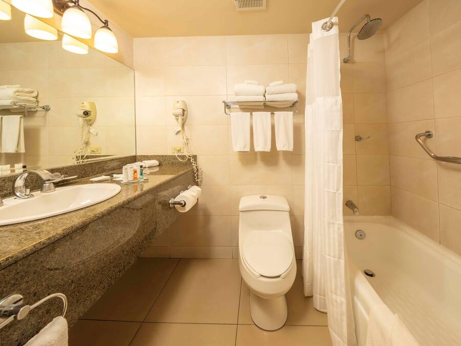 Ein Badezimmer mit Waschbecken, Toilette und Dusche. Handtücher und ein Fön befinden sich an der Wand.