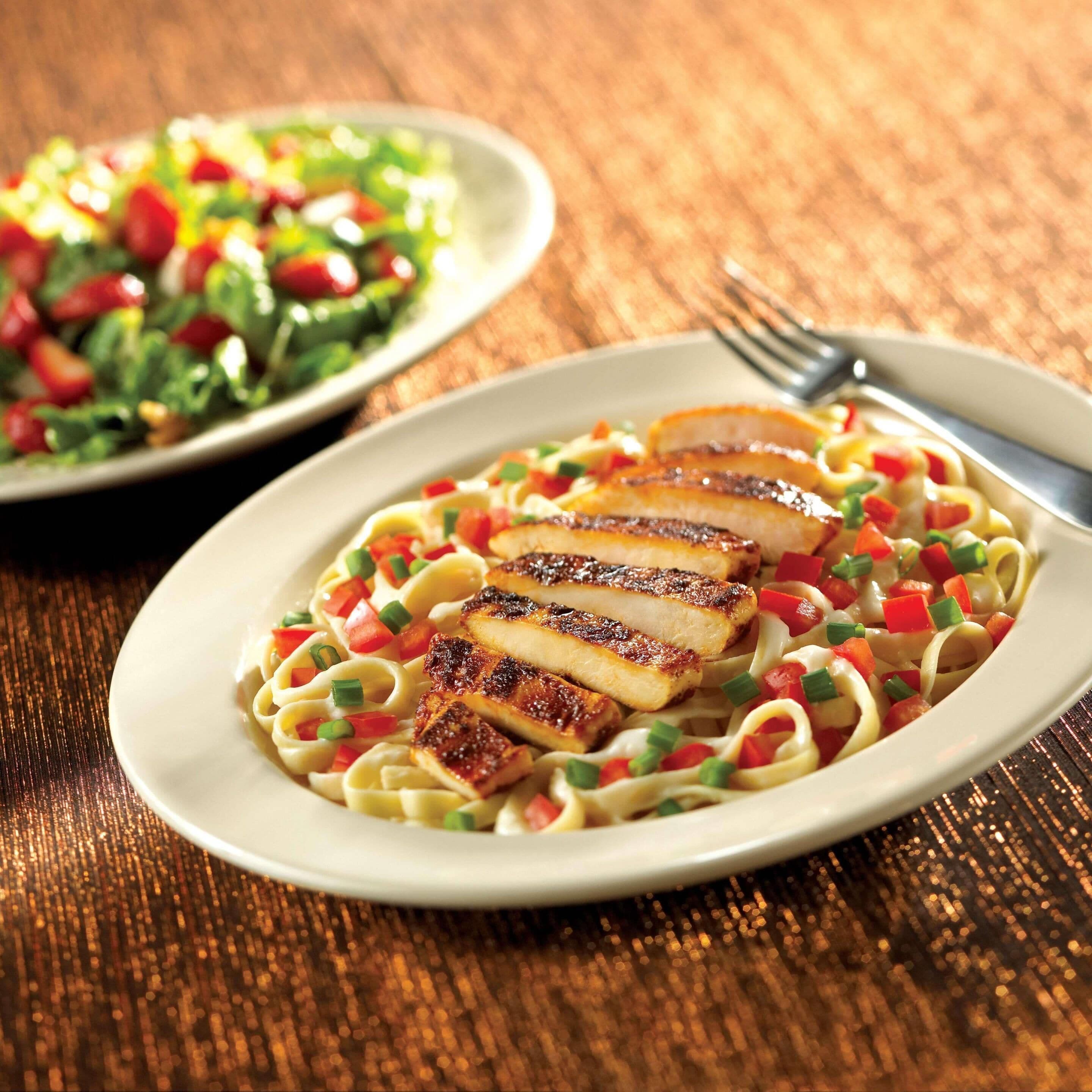 Ein Teller Pasta mit gegrilltem Hähnchen und gewürfelten Gemüse.