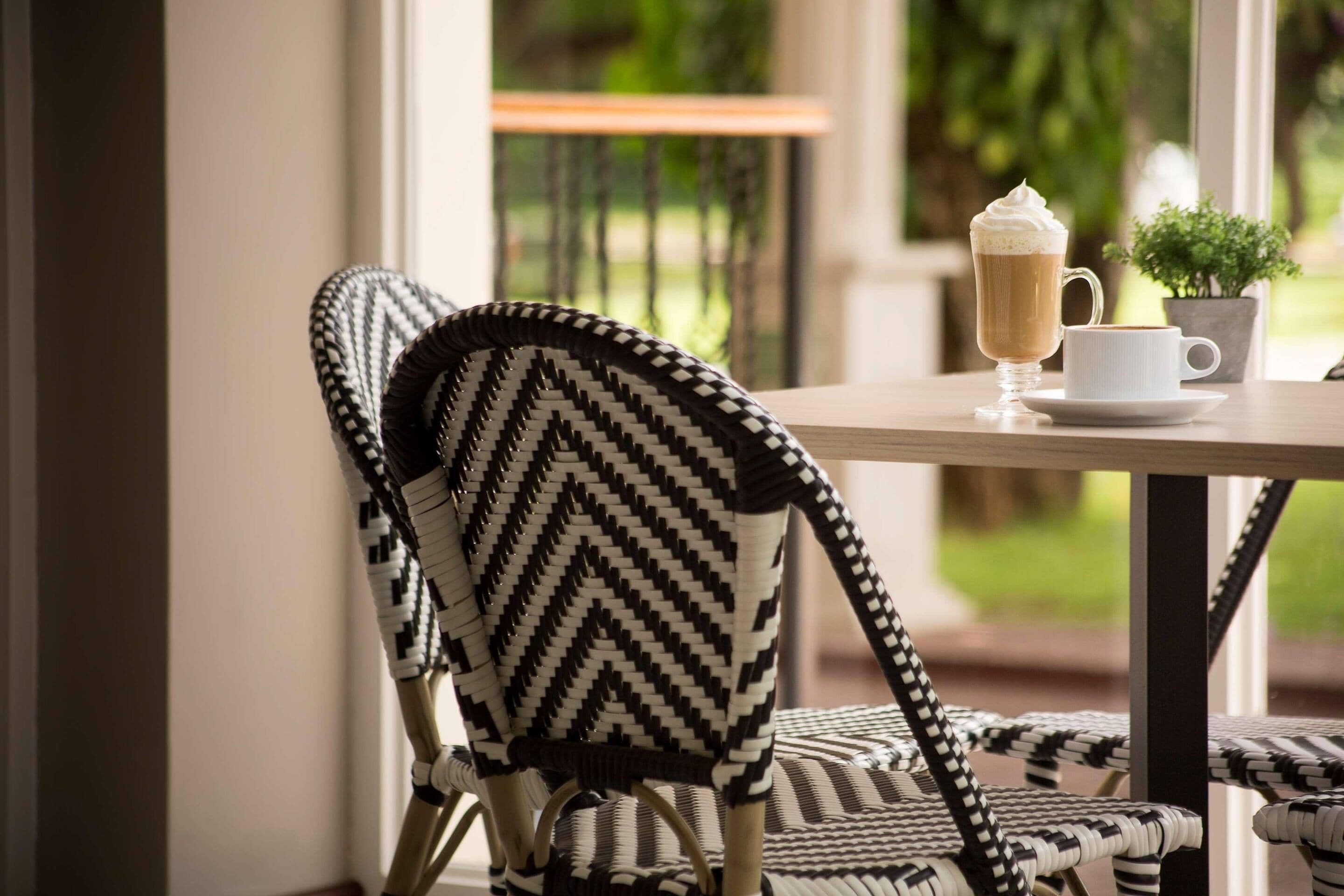 A chair with a black and white chevron pattern, a table with a white cup and a glass of coffee, and a small potted plant.