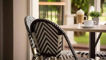 Una silla con estampado geométrico blanco y negro, una mesa con una taza blanca y una taza de café, y una pequeña planta en maceta.