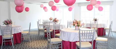 Una habitación con varias mesas y sillas, decorada con farolillos de papel rosa y centros de mesa florales.