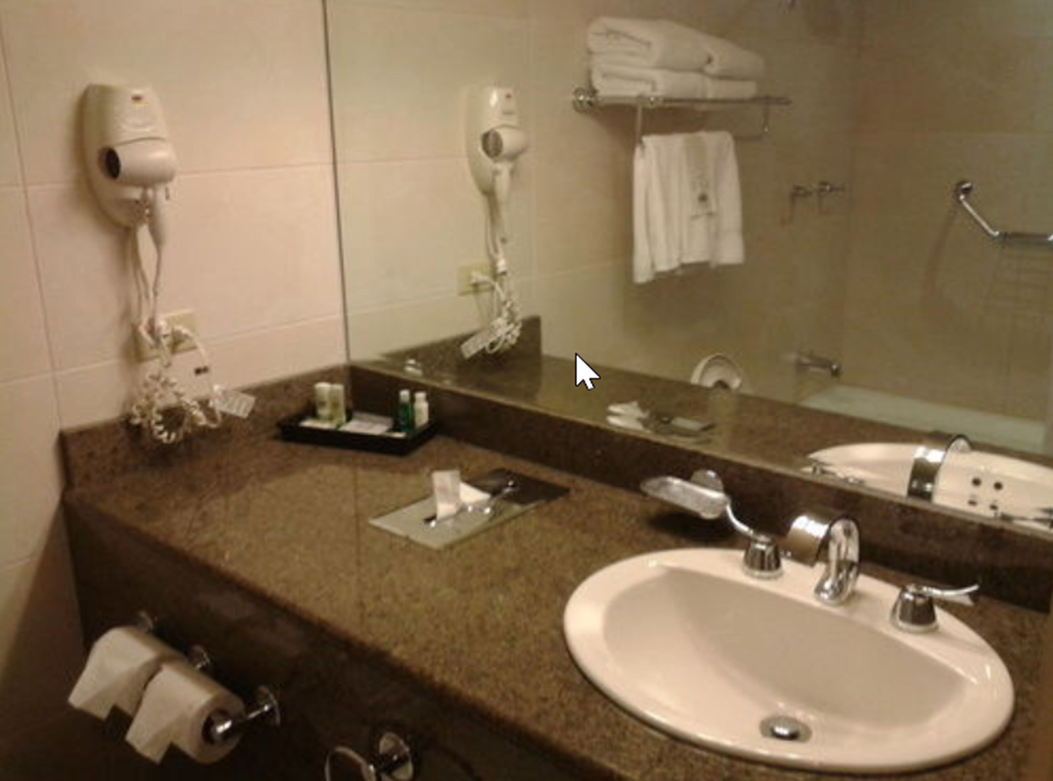 Un baño con lavamanos, espejo, toallero y secador de pelo.