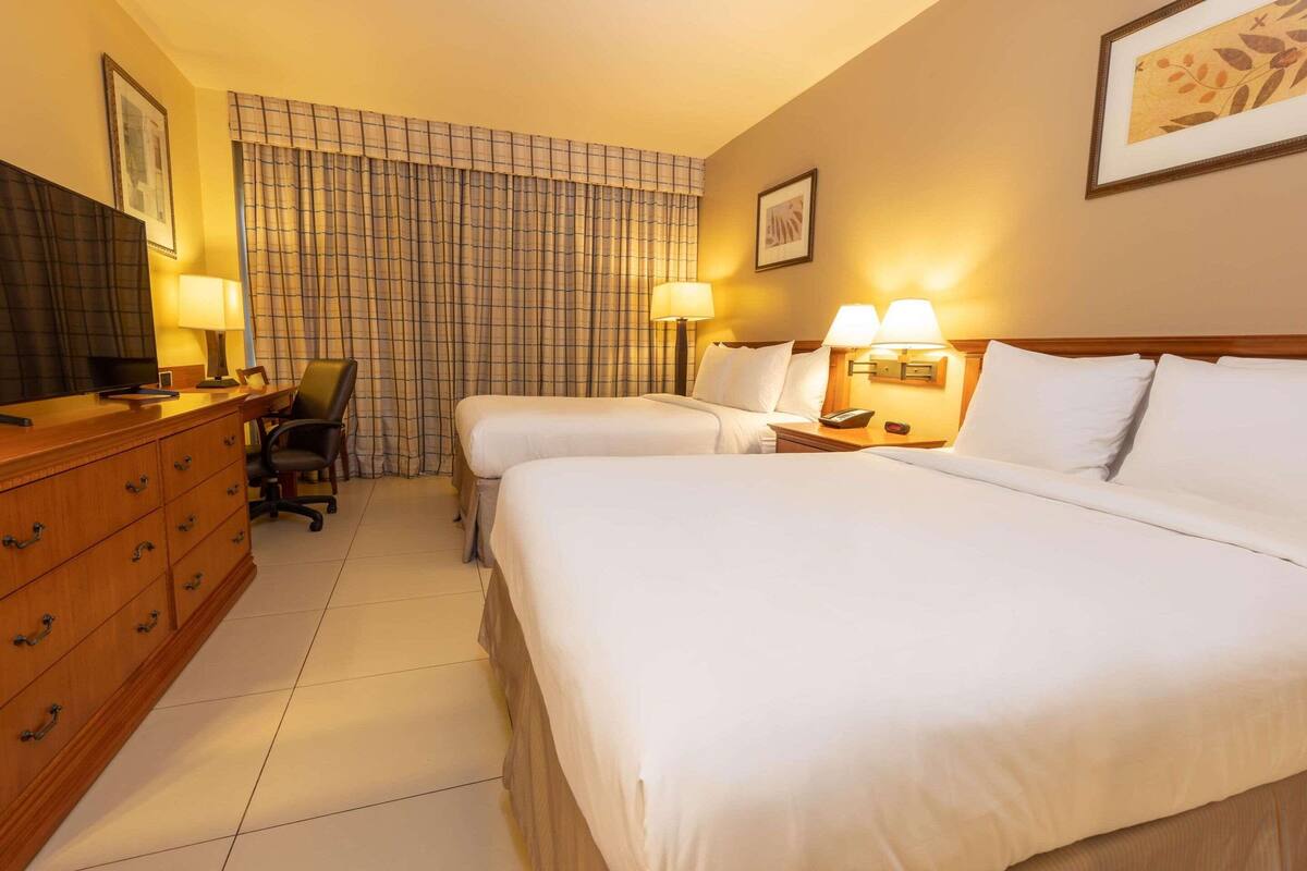 Une chambre d’hôtel avec deux lits, un bureau avec une chaise, une commode et deux lampes de chevet.