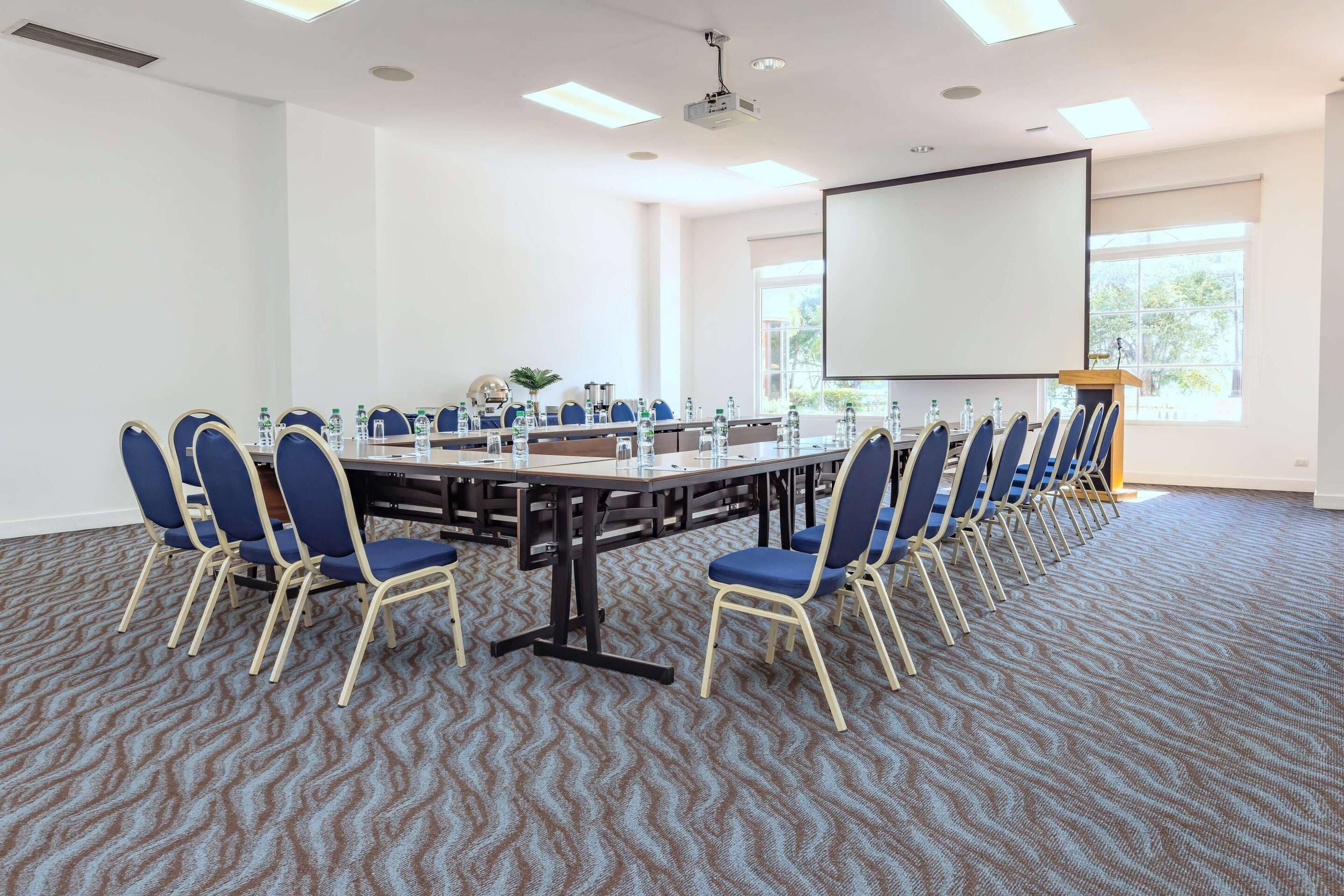 Un salón de conferencias con una gran mesa, sillas, un proyector y una pantalla.