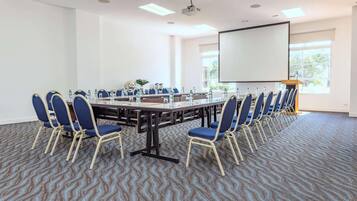 Un salón de conferencias con una gran mesa, sillas, un proyector y una pantalla.