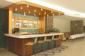 Una zona de bar con mostrador, taburetes y un área de estar con mesas y sillas.