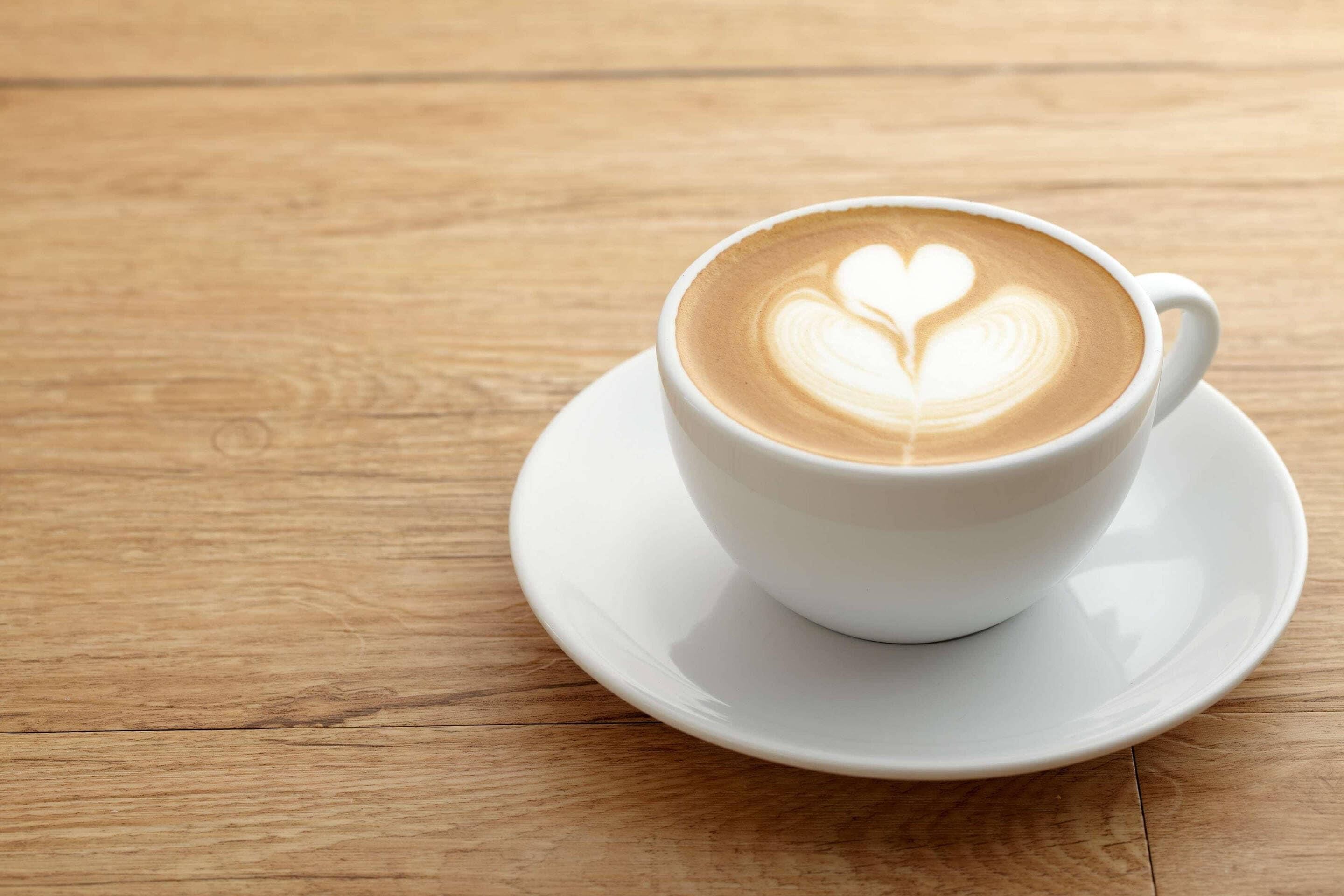 A white cup of coffee with a heart-shaped latte art on a wooden table.