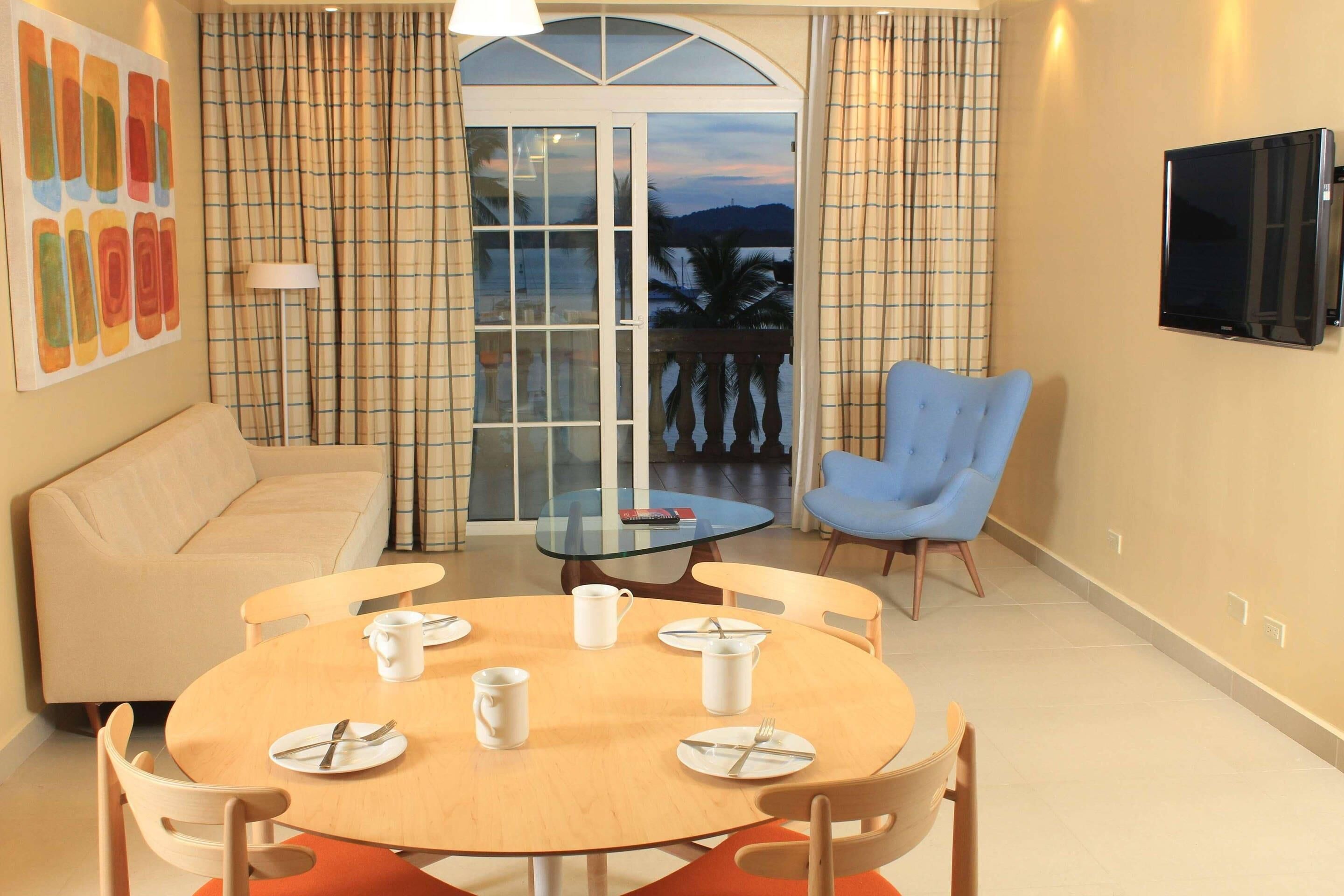 A modern living room with a round dining table, a sofa, a blue armchair, and a TV mounted on the wall.