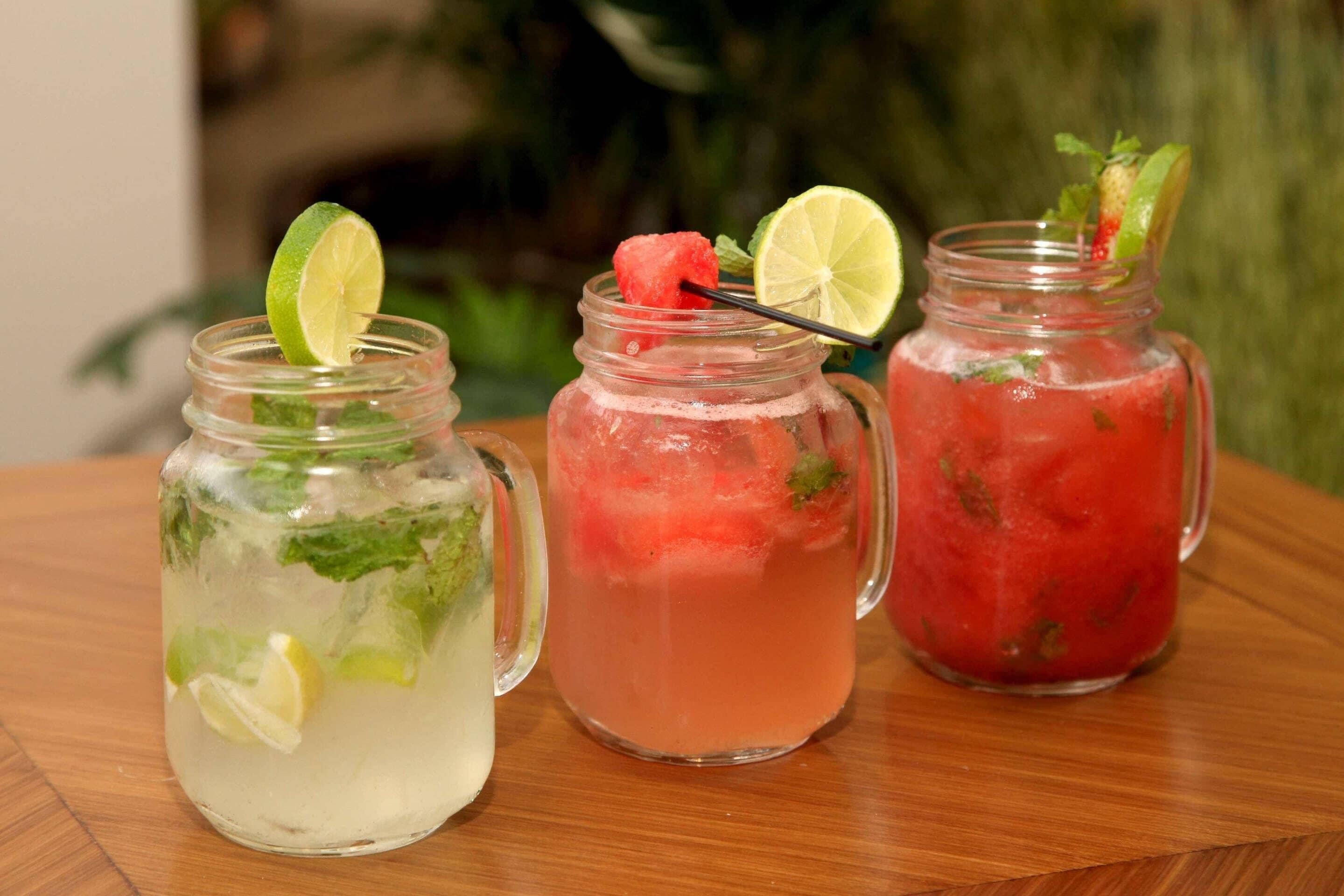 Three glass jars with different colored beverages, each garnished with a lime slice and mint leaves.