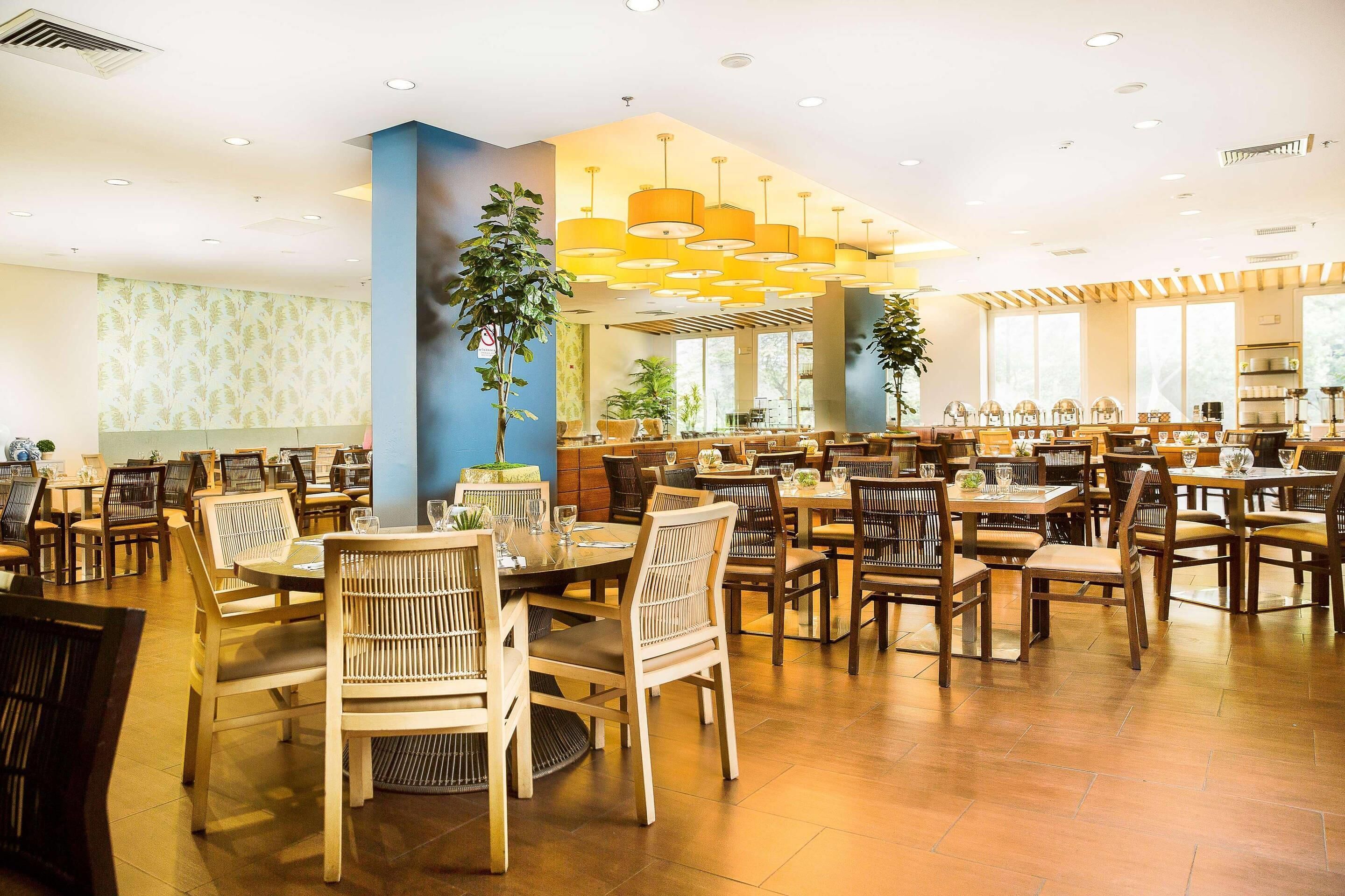 Un vaste espace dédié à la salle à manger, avec de nombreuses tables et chaises, de grandes fenêtres et des luminaires modernes.