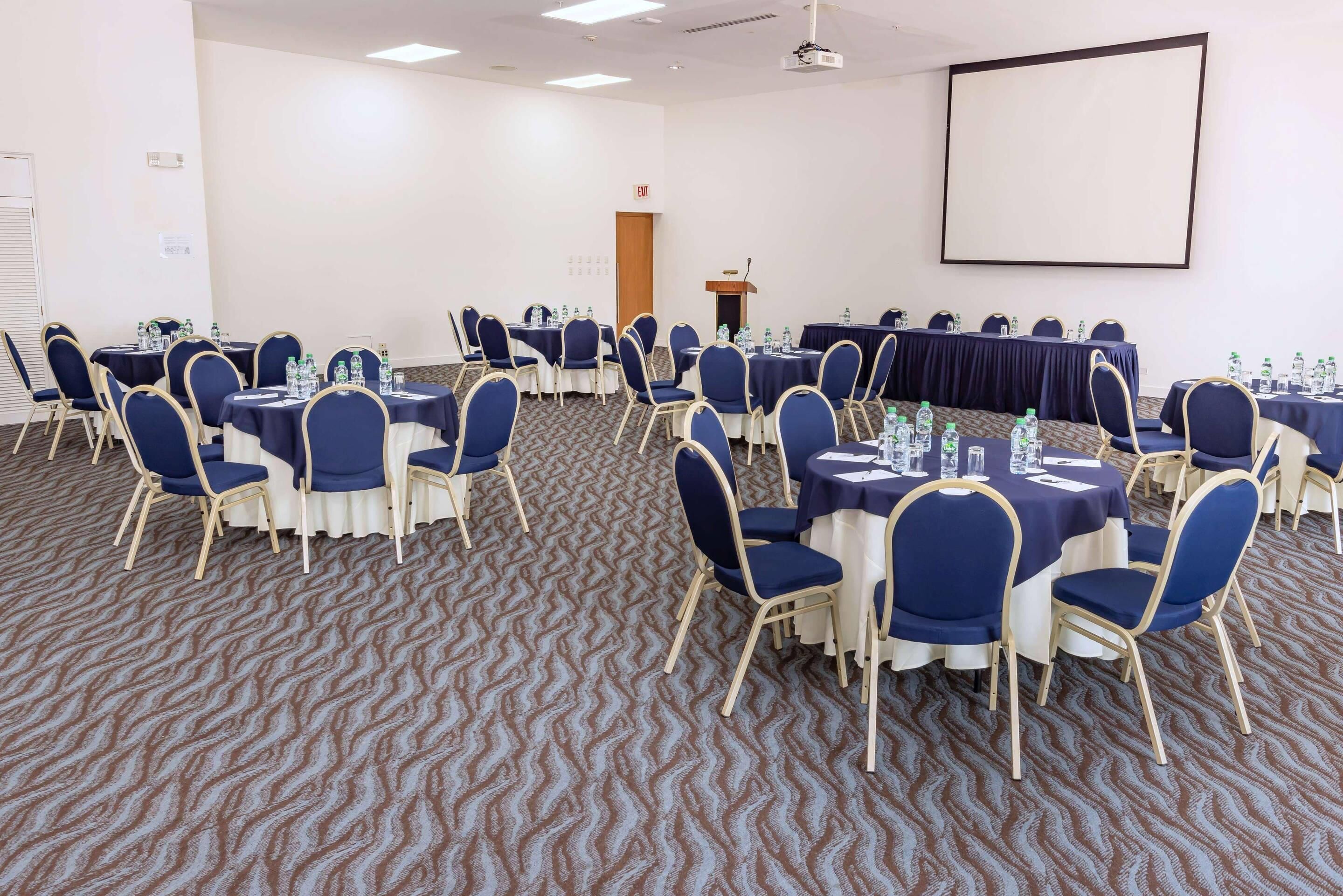 A conference room with round tables, blue chairs, and a projector screen.