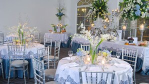 Un comedor formal con mesas redondas, manteles blancos y detalles de encaje azul.