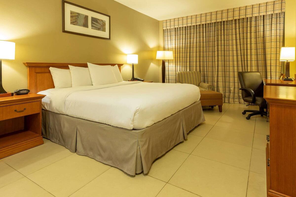 Une chambre d’hôtel avec un grand lit, deux tables de chevet avec des lampes, une chaise, un bureau et un rideau.