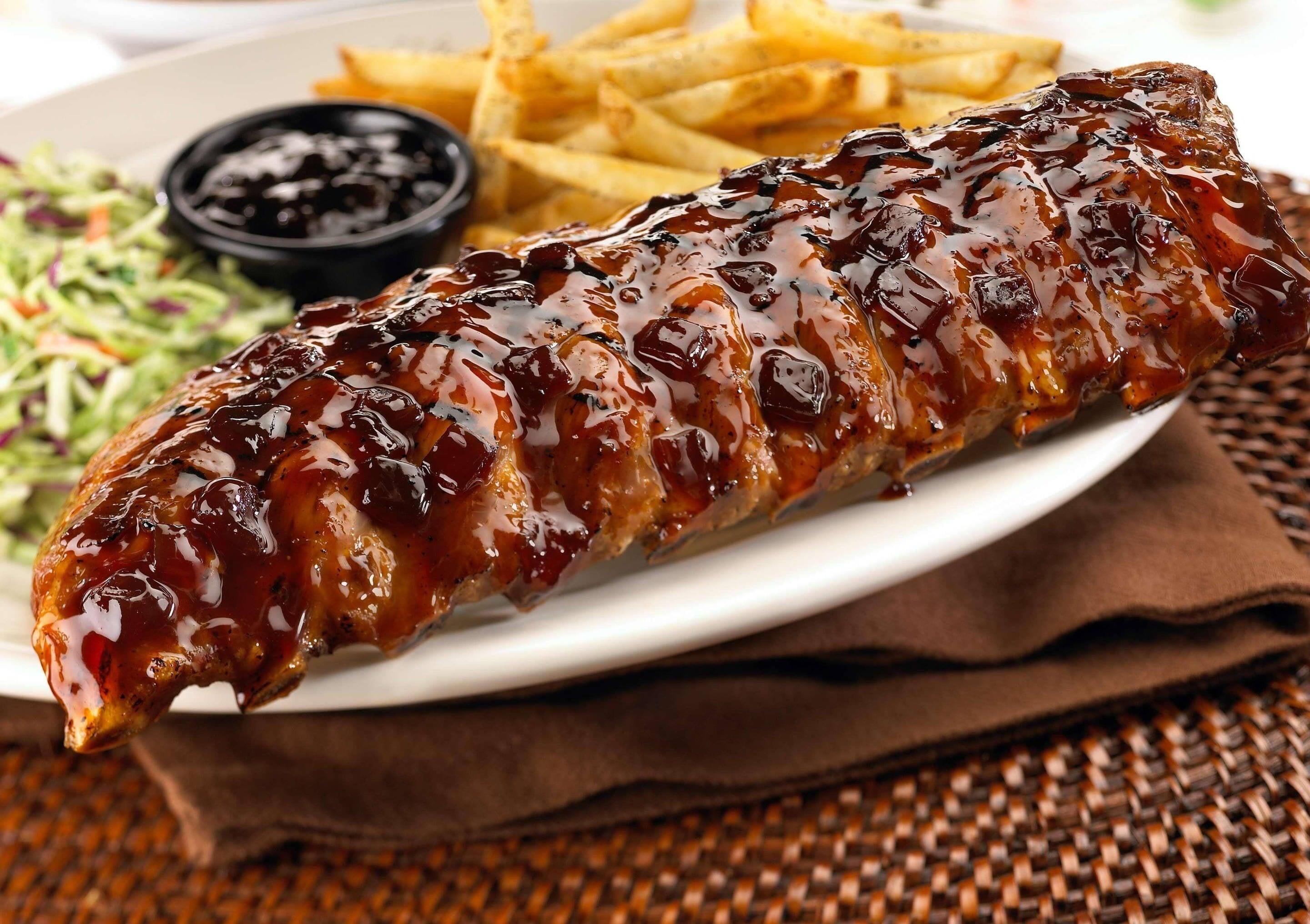 Un plato con costillas a la parrilla, una guarnición de papas fritas y un pequeño recipiente con salsa.