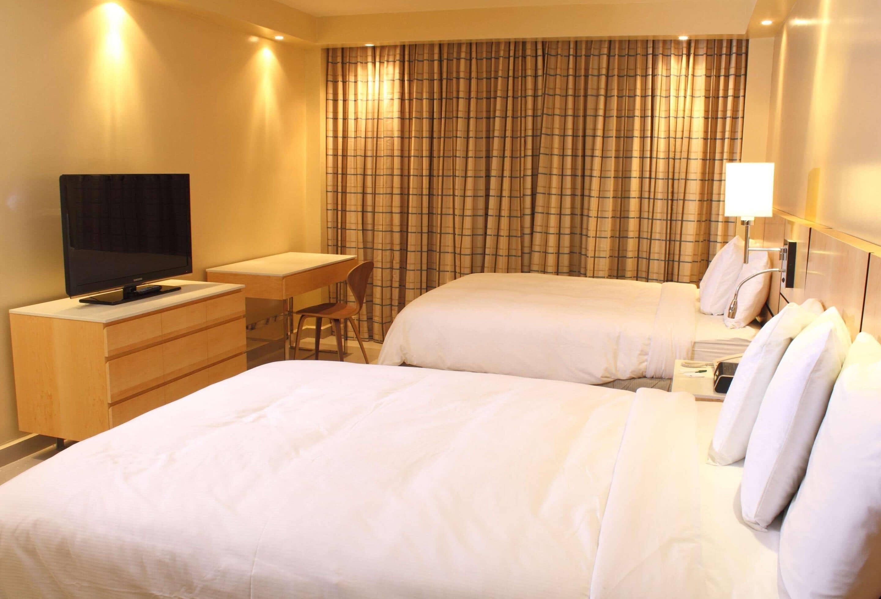 A hotel room with two beds, a desk, a television, and a window with curtains.