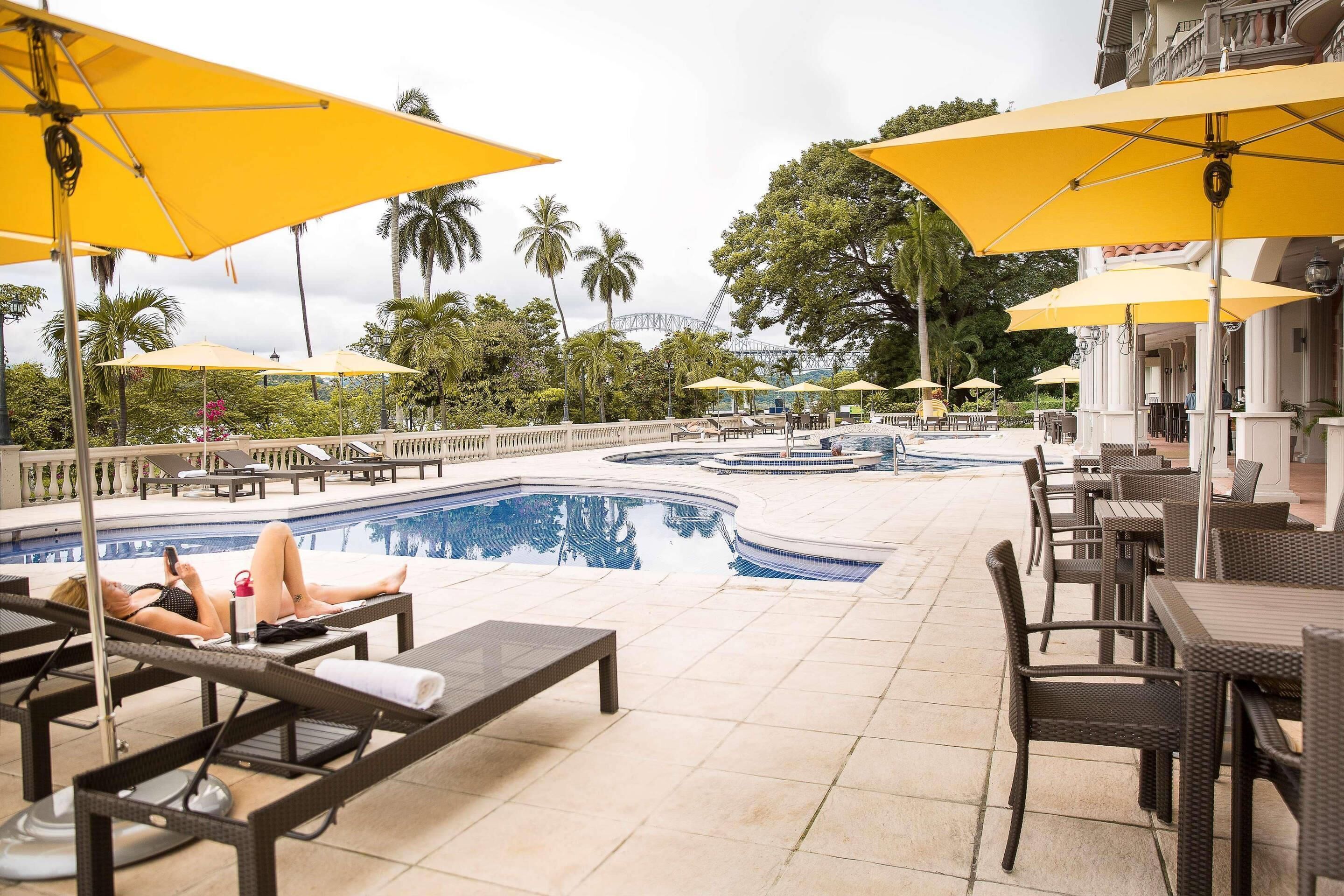 A poolside area with lounge chairs, yellow umbrellas, and a view of a bridge in the background.